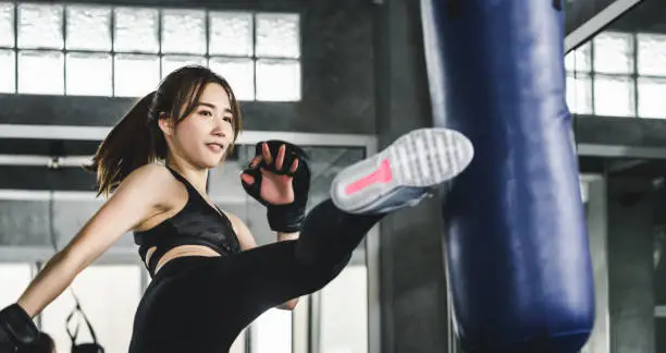 Young asian athlete fitness woman with boxing gloves doing kick boxing training in sport gym