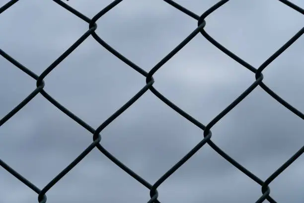 Details of a wire-mesh fence in front of the dark and cloudy sky - security concept