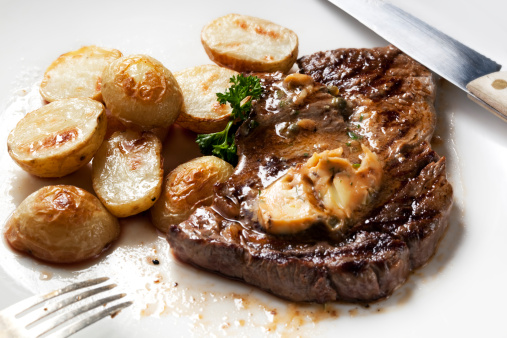 Tasty beef stakes in a pan with baked potato and spinach, on a home or restaurant kitchen table