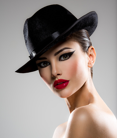 Ð¡lose-up portrait of a woman in a black hat  with red lips posing at studio