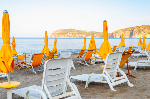 istock White plastic and metal construction with yellow fabric deckchairs together with yellow umbrellas on the sand beach of Tyrrhenian sea with mountains on background in Italy 1191495970