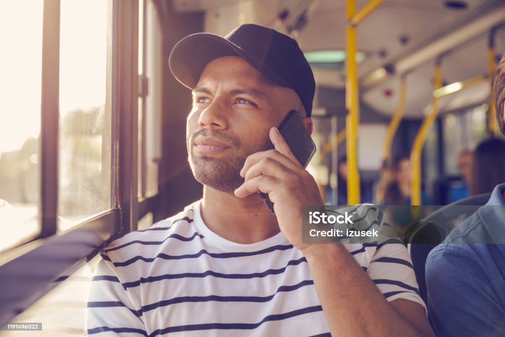 Man talking on mobile phone in bus Mid adult man talking on mobile phone while traveling in bus. Male is looking away while commuting by public transport. He is sitting by window. 30-34 Years Stock Photo