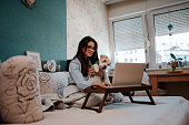 Beautiful woman using laptop with dog in her lap at home.