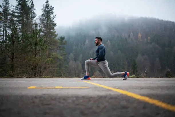 Full Length Athlete man with beard stretching outdoor in front of foggy hill, autumn outdoor workout