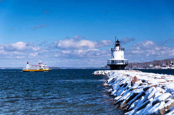 spring point ledge lighthouse portland maine A passenger ferry traveling near the snow covered spring point ledge lighthouse in portland maine on a blue sky winter day. casco bay stock pictures, royalty-free photos & images