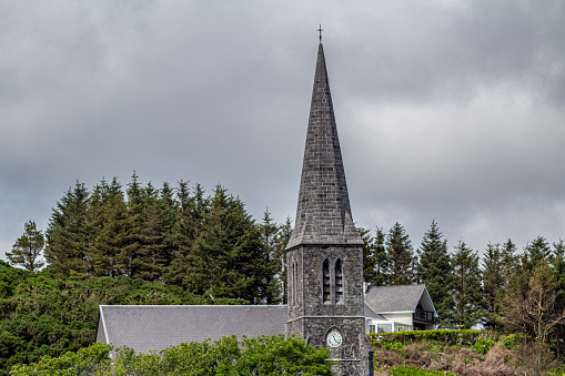 St. Joseph's church tower with its bell tower and clock with trees in the background, spring day with an overcast sky in Clifden, province of Connacht, Ireland