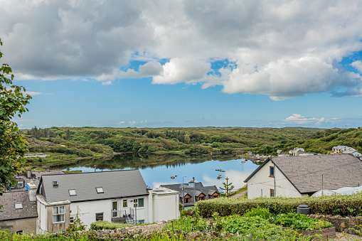 Clifden Bay surrounded by green vegetation seen from a hill with houses, mirror reflection in the water, spring day with a blue sky and abundant clouds in the Connacht province, Ireland