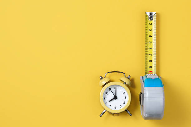 istock Measuring tape and alarm clock isolated over yellow bakground. Carpenter and Construct concept. 1191509151