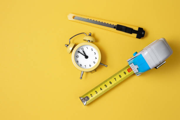 istock Measuring tape, cutter knife and clock isolated over yellow bakground. Carpenter and Construct concept. 1191509154