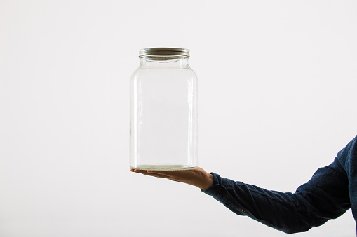 Close up of person hand holding an empty glass jar isolated over white background with copy space.