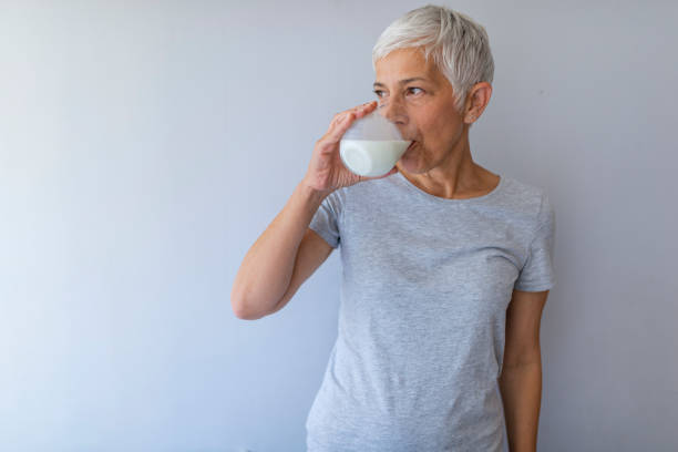 mujer mayor sosteniendo un vaso de leche en casa. - mujer bebiendo leche fotografías e imágenes de stock