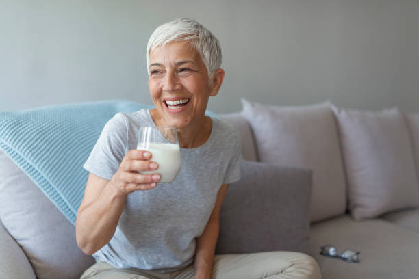 feliz mujer mayor divirtiéndose mientras bebe leche en casa. - mujer bebiendo leche fotografías e imágenes de stock