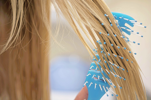 Young girl combing her wet blond hair with a blue comb