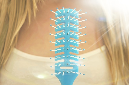 Closeup blue comb, young girl with wet blond hair on a blurred background