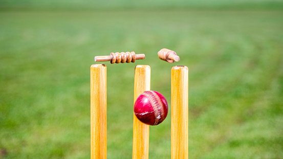 Close-up photo of a cricket ball hitting the stumps and knocking off the bails.