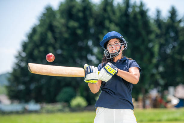 Female cricket player hitting the ball with a bat Front view photo of a female cricket player in mid-stroke while batting the ball. cricket player photos stock pictures, royalty-free photos & images