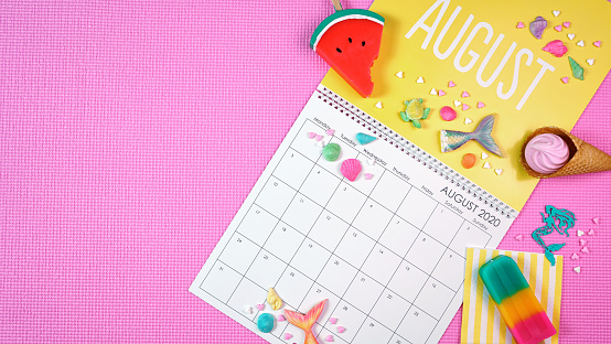 On-trend 2020 calendar page for the month of August modern flat lay with seasonal food, candy and colorful decorations in popular pastel colors. Copy space. One of a series for 12 months of the year.