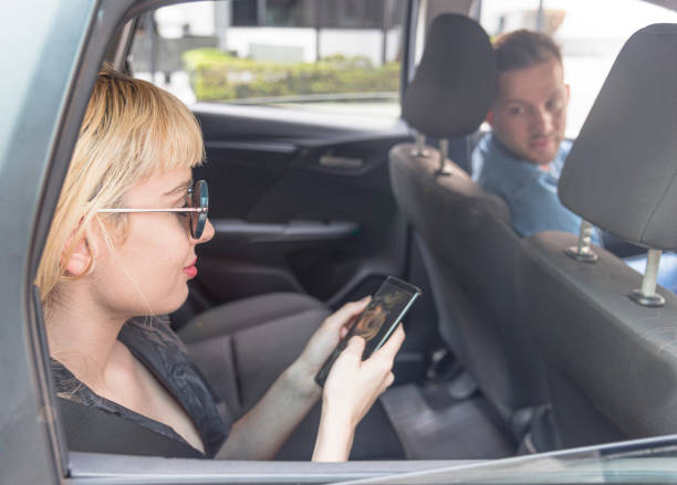 istock Young woman browsing on her smartphone inside parked car with driver waiting. 1191522945