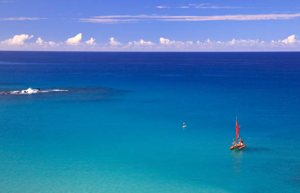 A red sailboat in a stunning turquoise tropical sea.