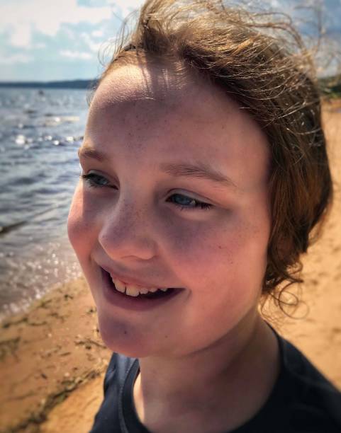 Cute smiling girl enjoying the breeze on Lake Michigan. Cute smiling and happy child(10 years old), enjoying the summer Lake breeze on Lake Michigan in The Upper Peninsula of Michigan at a beach in Gladstone. The portrait is a close-up of the little girls freckled blue-eyed face. Lake Michigan shore line and the sandy beach can be seen behind her. gladstone michigan photos stock pictures, royalty-free photos & images
