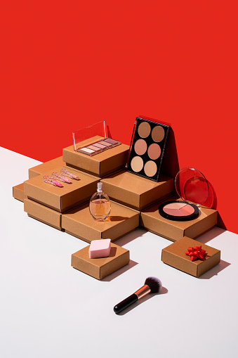Kraft paper gift boxes and makeup accessories flat lay on red and white background