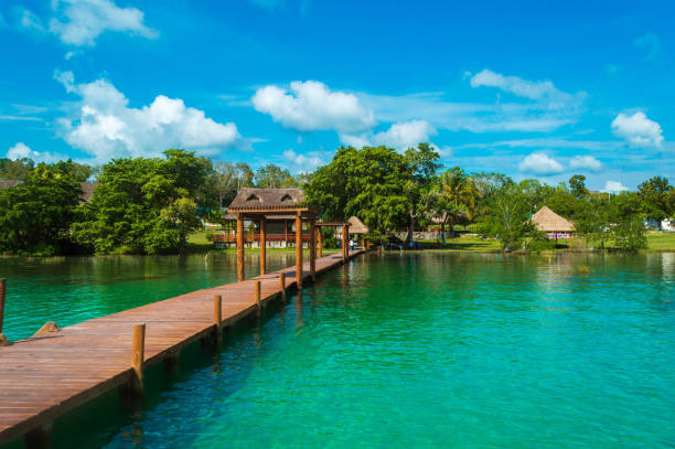 Wooden pier in the lagoon of the seven colors with beautiful scenery. People enjoying the crystal clear water of the Bacalar lagoon, Quintana Roo, Mexico. Palapa at the end of the pier in the lagoon of Bacalar. Tourist place in Bacalar. Travel concept muelle de madera en la laguna de los siete colores con hermoso paisaje. gente disfrutando del agua cristalina de la laguna de bacalar, quintana roo, méxico. palapa al final del muelle en la laguna de bacalar. lugar turístico en bacalar. concepto de viaje