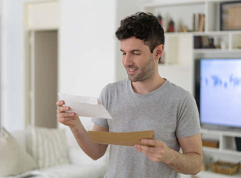 Young man at home reading very cheerfully a letter he just received at home - Lifestyles