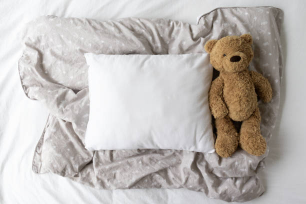 Blank white rectangle cushion laying on a gray patterned duvet with a white background and child's teddy- nursery pillow mockup