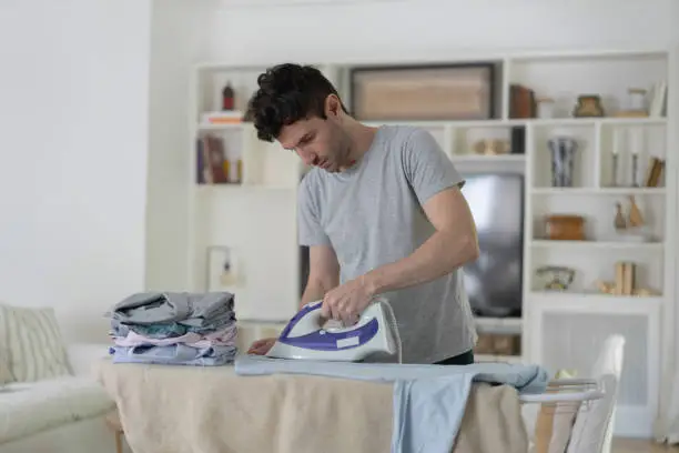 Latin american man at home ironing his button down shirts - Domestic lifestyles