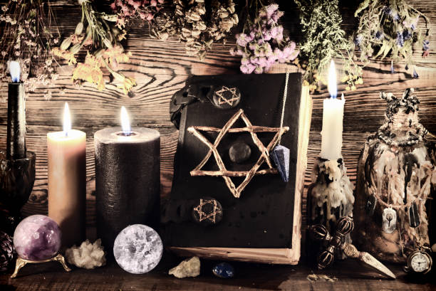 Creepy still life with burning candles, pentagram book, elixir bottles and dry herbs on witch table. Esoteric, wicca and occult background, fortune telling and divination ritual, mystic concept