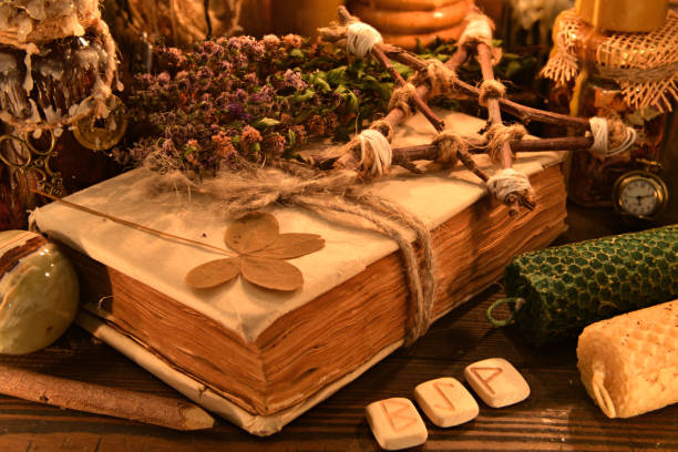 istock Old book with four-leaf clover, candles, herbs and runes on witch table. 1191563809