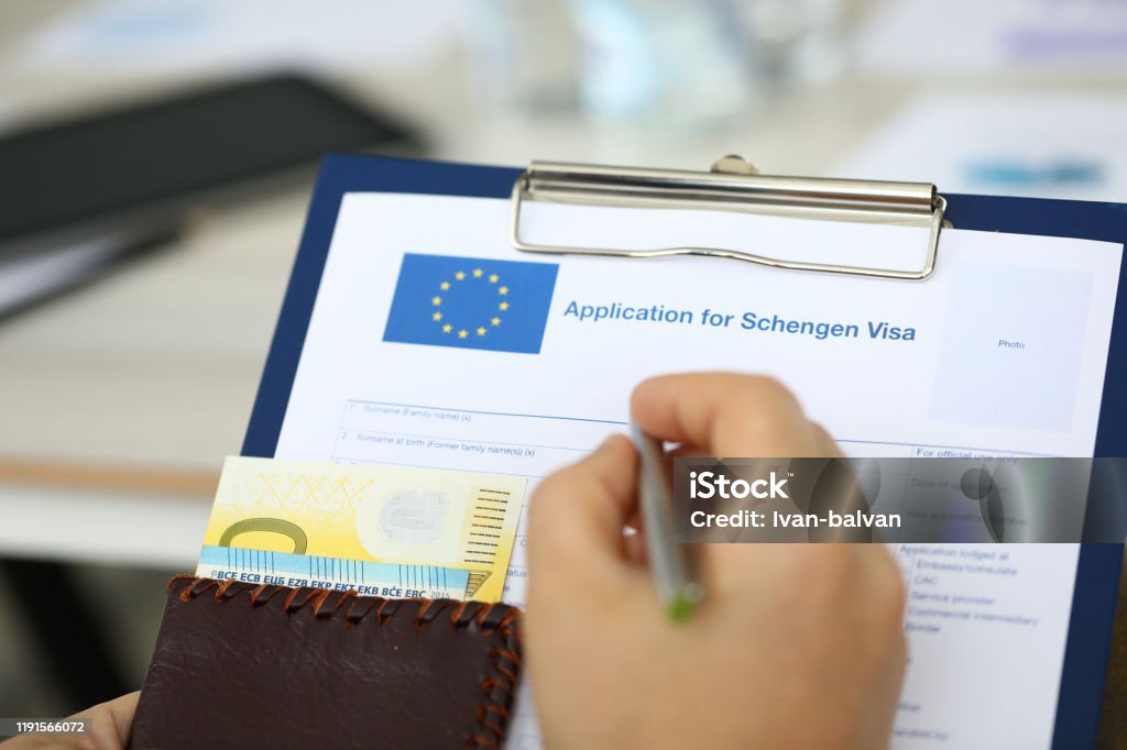Man filling questionnaire form Focus on male hand holding paper folder, passport with money and answering to questions posed in application for schengen visa. Travelling abroad and immigration concept. Blurred background Schengen Agreement Stock Photo