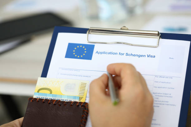 Man filling questionnaire form Focus on male hand holding paper folder, passport with money and answering to questions posed in application for schengen visa. Travelling abroad and immigration concept. Blurred background schengen agreement stock pictures, royalty-free photos & images