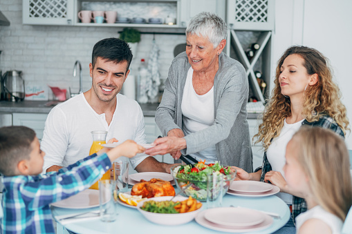 Photo of a young happy family having lunch or dinner together. Grandmother serving.