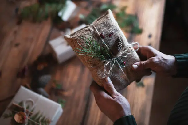 Unrecognizable male hands wrapping Christmas presents with natural materials, plastic free, organic wrapping with paper.