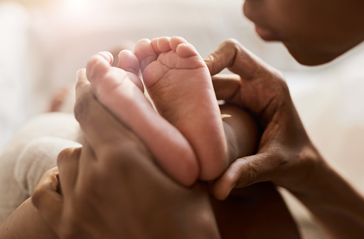 Close up portrait of African-American woman holding tiny feet of cute baby in sunlight, copy space