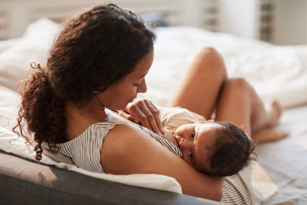 madre joven amamantando bebé en casa - alimentar fotos fotografías e imágenes de stock