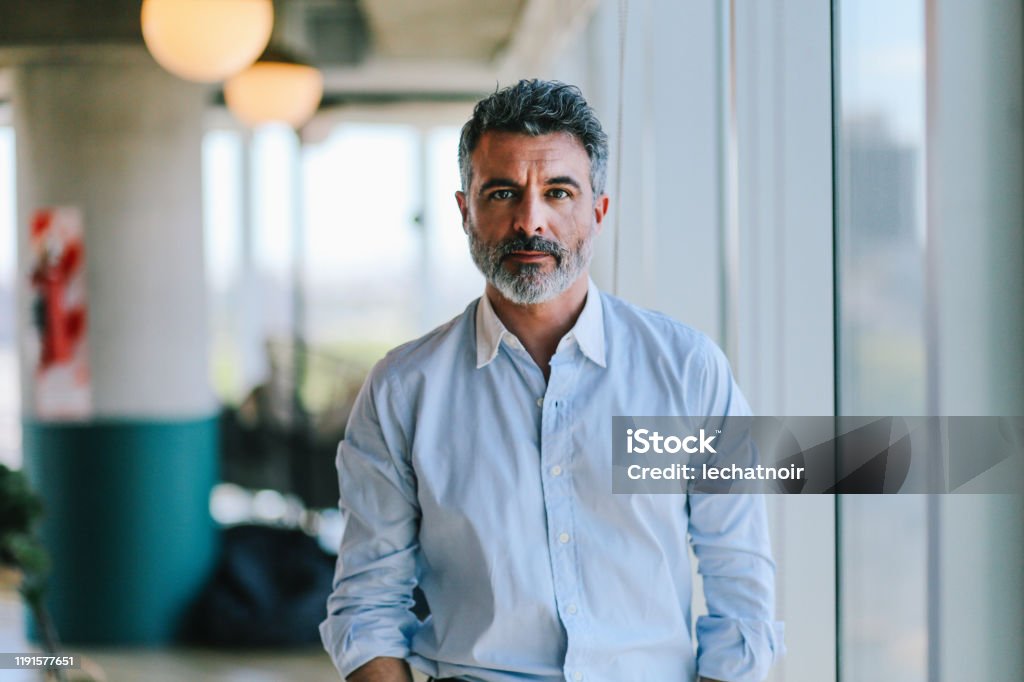 Portrait of a businessman in the Buenos Aires office Portrait of a handsome businessman relaxing by his office window in Buenos Aires, Argentina, looking at the camera. Men Stock Photo