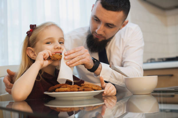 istock Little kid and her father eating biscuits at the kitchen while father is cleaning her face. Father and daughter in the morning at kitchen eating. 1191583803