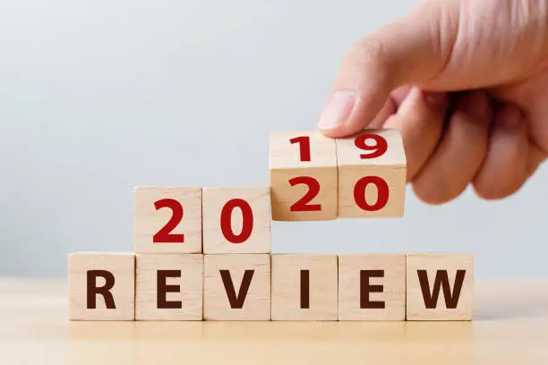 Photo of 2020 review concept. Hand flip wood cube change year 2019 to 2020 and the word REVIEW on wooden block on wood table