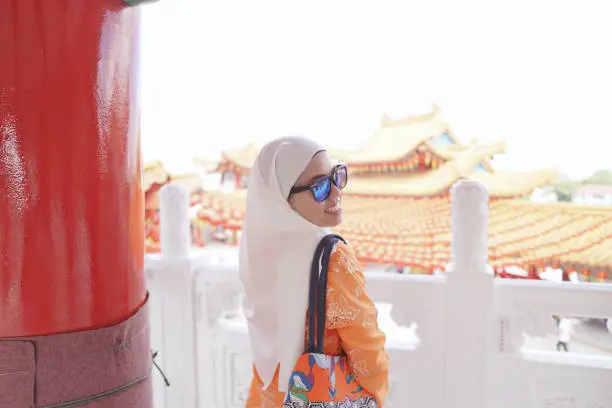 Photo of A confident muslim lady visiting a famous attraction, Thean Hou Chinese Temple in Kuala Lumpur on a very bright sunny day.