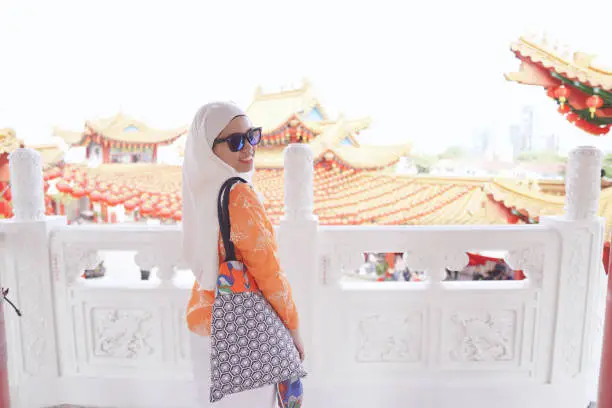 Photo of A confident muslim lady visiting a famous attraction, Thean Hou Chinese Temple in Kuala Lumpur on a very bright sunny day.