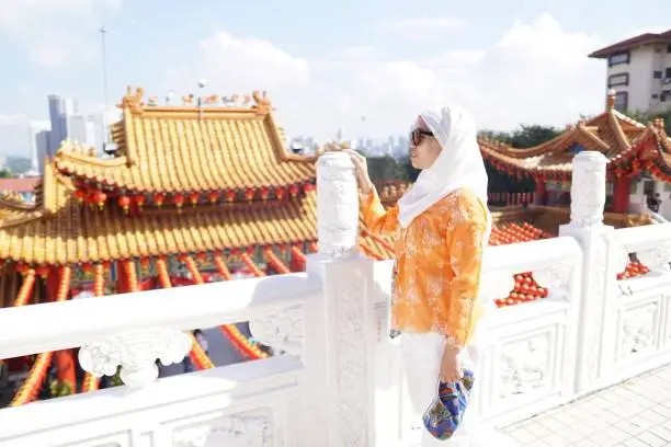 Photo of A confident muslim lady visiting a famous attraction, Thean Hou Chinese Temple in Kuala Lumpur on a very bright sunny day.