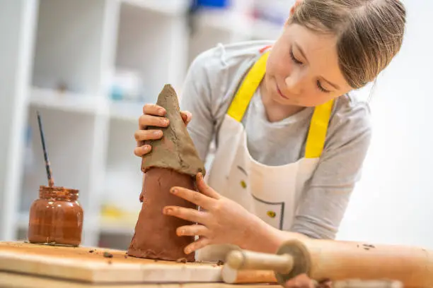 Girl making birdhouse with clay in classroom.