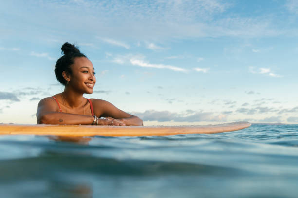 молодая женщина отдыхает на доске для серфинга в ожидании волны - tropical climate water leisure activity holidays стоковые фото и изображения