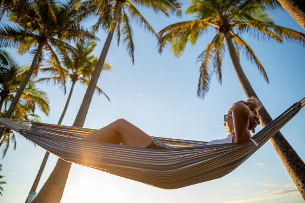 istock Woman watching sunrise from hammock hanging on palm trees 1191594480