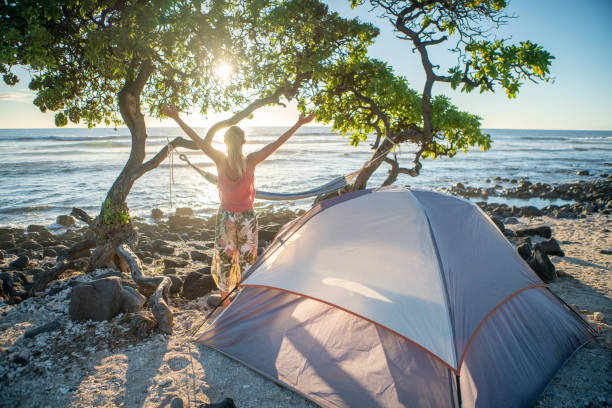 giovane donna campeggio sulla spiaggia si spalanca le braccia davanti alla tenda al tramonto - big island isola di hawaii foto e immagini stock