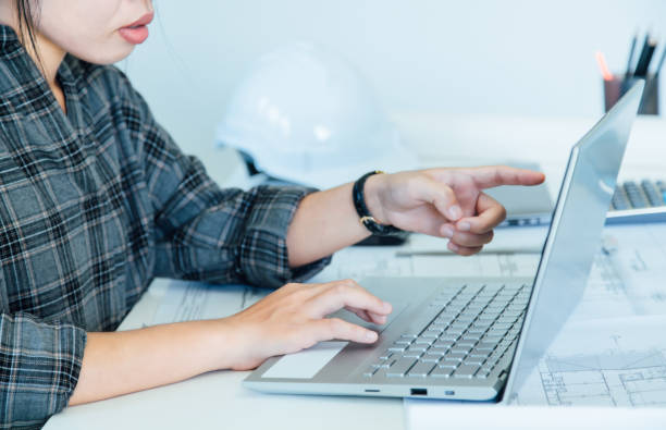 istock Woman designer architect sitting and pointing drawing project working on laptop with a blueprint and Model in the office 1191597735
