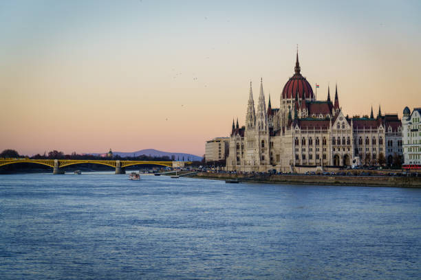 Beautifuĺ winter twilight over the Parliament Building of Hungary on the Riverside if the Danube River. Tourist boats cruising on the Danube River, Tourists walking along the waterfront promenade, visiting the HungaryParliament Building on the Pest Side of Budapest. Budapest, Hungary, Europe