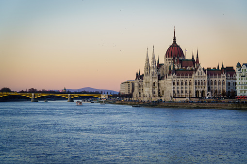 Beautifuĺ winter twilight over the Parliament Building of Hungary on the Riverside if the Danube River. Tourist boats cruising on the Danube River, Tourists walking along the waterfront promenade, visiting the HungaryParliament Building on the Pest Side of Budapest. Budapest, Hungary, Europe